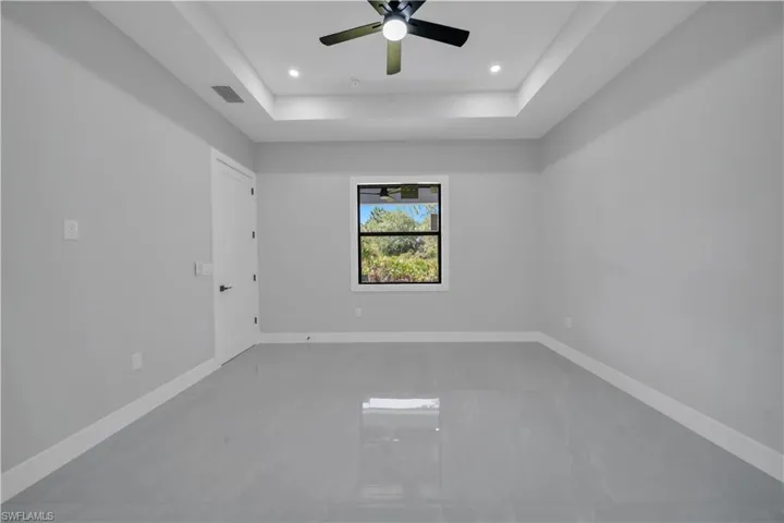 Empty room featuring a raised ceiling, ceiling fan, baseboards, and recessed lighting