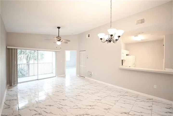 Spacious living area featuring polished tile flooring, sliding glass doors to a balcony, a ceiling fan, and a chandelier