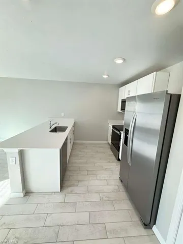 Kitchen with a peninsula, stainless steel appliances, white cabinets, and light stone countertops