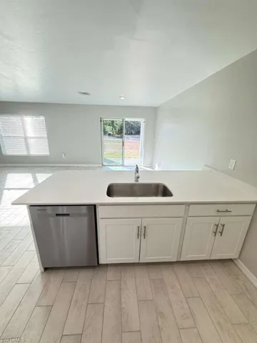 Kitchen featuring stainless steel dishwasher, white cabinetry, light wood-type flooring, and a peninsula