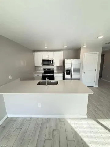 Kitchen with white cabinetry, appliances with stainless steel finishes, a peninsula, light wood-style flooring, and light stone counters