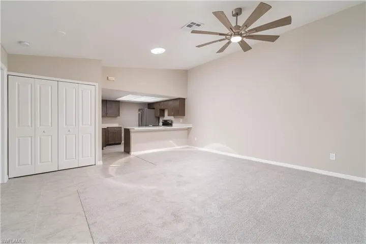 Unfurnished living room with visible vents, baseboards, ceiling fan, light carpet, and vaulted ceiling