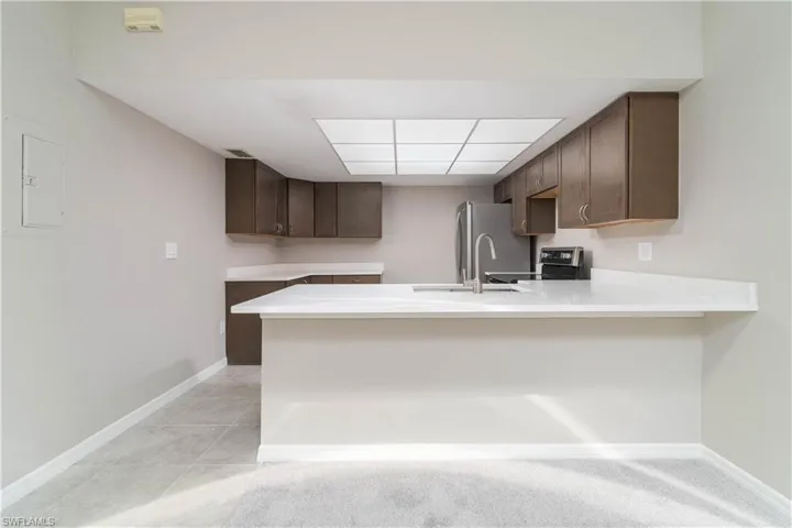 Kitchen featuring light countertops, baseboards, a sink, a peninsula, and dark brown cabinets