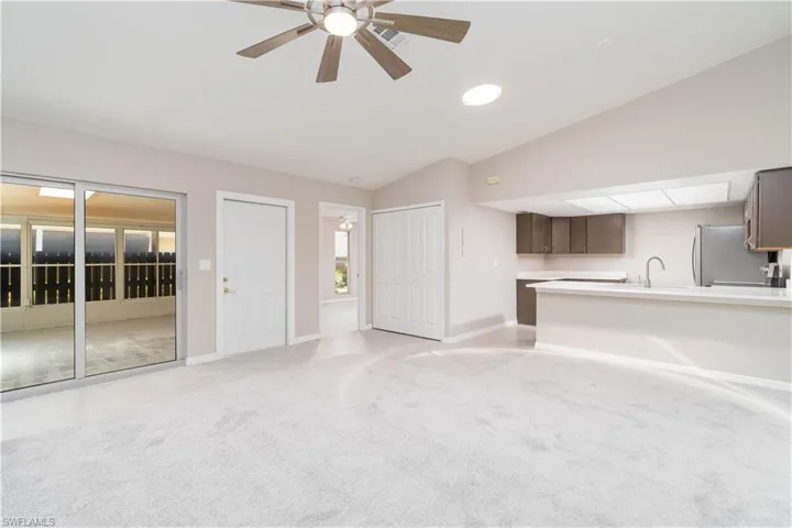 Unfurnished living room with vaulted ceiling, a sink, visible vents, a ceiling fan, and light carpet