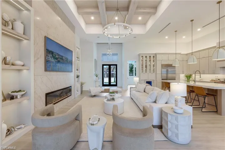 Living room with a fireplace, built in shelves, coffered ceiling, a chandelier, and light wood finished floors