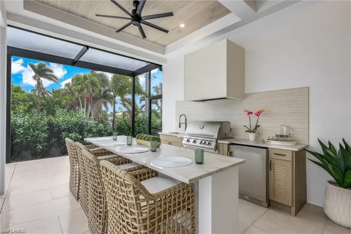 View of patio featuring exterior kitchen, ceiling fan, and glass enclosure