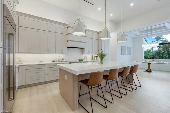 Kitchen featuring hanging light fixtures, light stone countertops, a kitchen island with sink, a breakfast bar area, and decorative backsplash