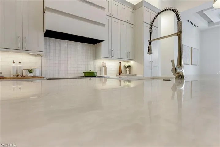 Kitchen view of premium range hood, decorative backsplash, and light stone countertops