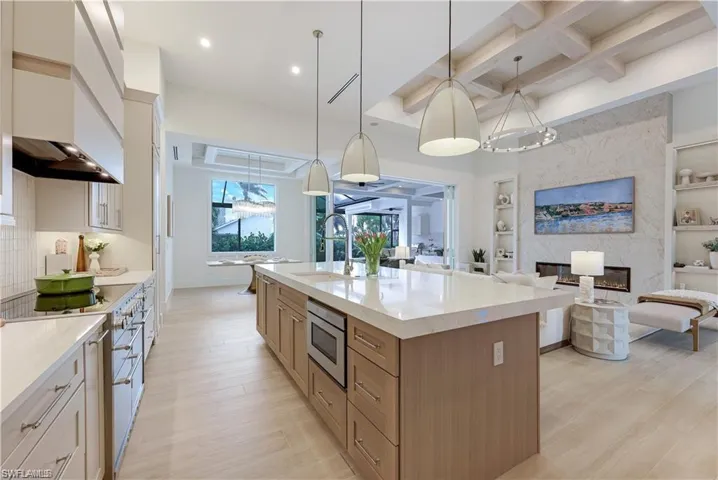 Two tone kitchen featuring dual tone cabinetry, open floor plan, hanging light fixtures, built in features, and coffered ceiling