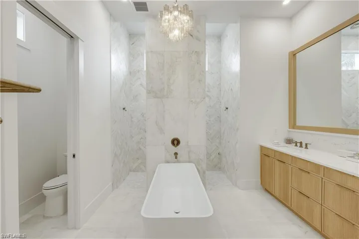 Full bath featuring suspended lighting, a freestanding tub, a marble finish shower, and vanity