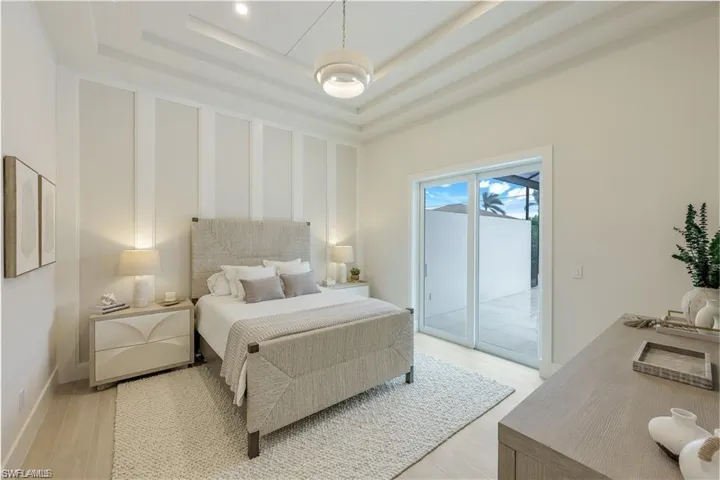 Bedroom with light wood finished floors, a raised ceiling, a decorative wall, and access to outside