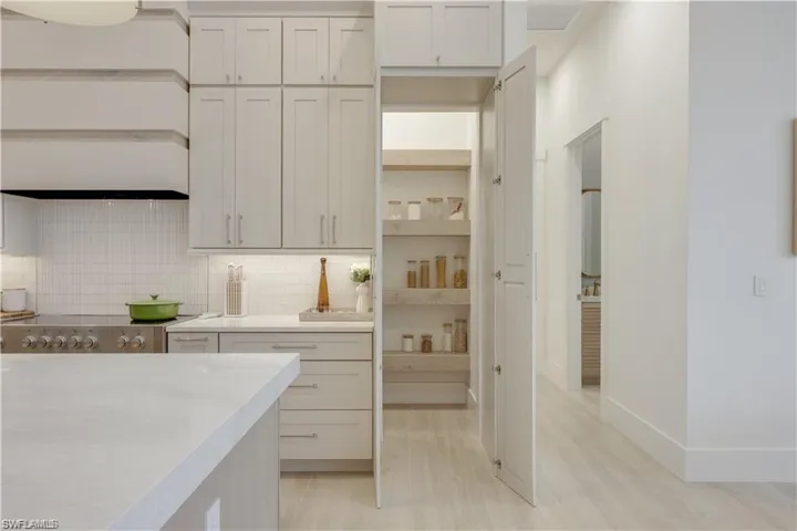 Kitchen featuring decorative backsplash, light stone countertops, open shelves, light wood-style flooring, and white cabinets