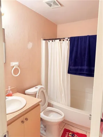 Bathroom with vanity, a textured wall, shower / tub combo with curtain, and light tile patterned flooring