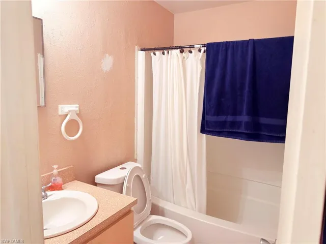 Bathroom with a textured wall, shower / bath combo with shower curtain, and vanity