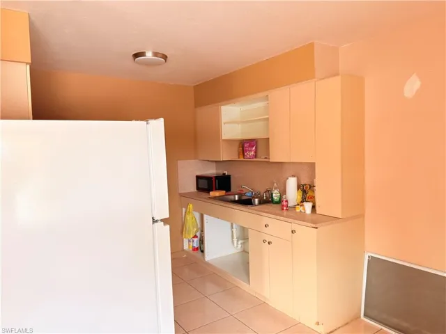 Kitchen with freestanding refrigerator, light countertops, decorative backsplash, open shelves, and black microwave