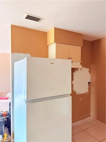 Kitchen featuring white refrigerator, light tile patterned flooring, a textured ceiling, and exhaust hood