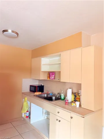 Kitchen with cream cabinets, open shelves, light countertops, tasteful backsplash, and light tile patterned flooring