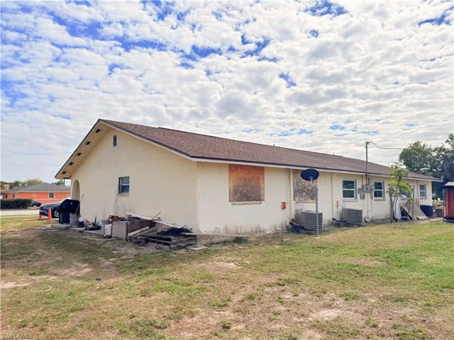 Back of property with stucco siding, a lawn, and roof with shingles