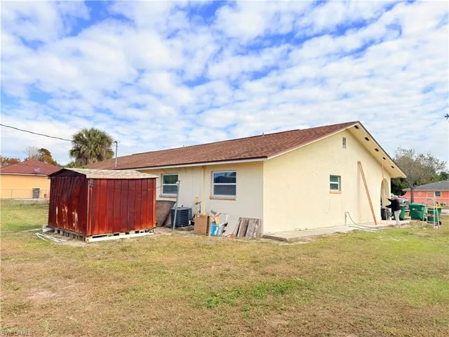 Back of house with a shed, a yard, stucco siding, and a shingled roof