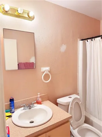 Full bath with shower / tub combo with curtain, vanity, and a textured wall