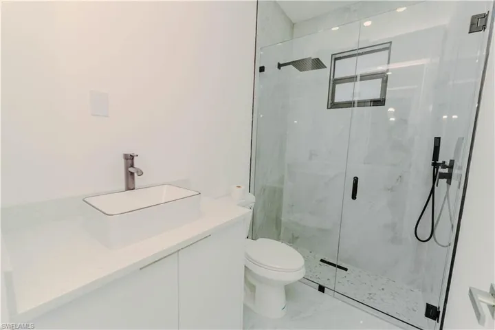 Full bath with a marble finish shower, toilet, marble finish floor, and vanity