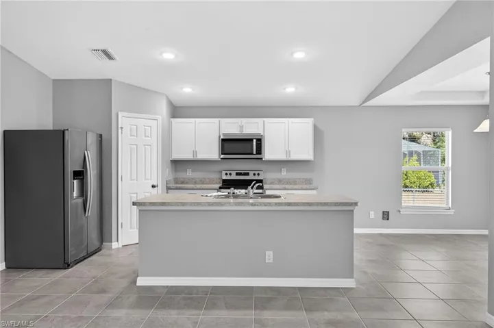 Kitchen with stainless steel appliances, light countertops, white cabinets, a kitchen island with sink, and light tile patterned floors