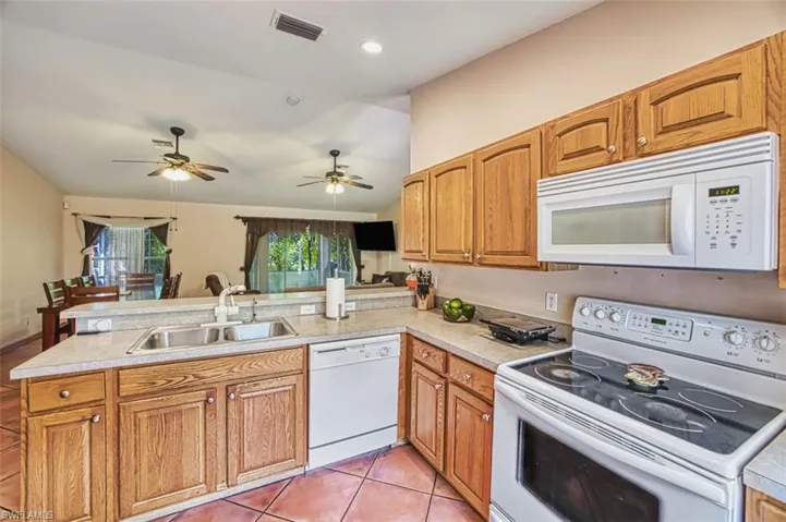 Kitchen featuring white appliances, vaulted ceiling, light countertops, brown cabinets, and a peninsula