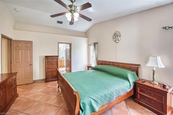 Bedroom featuring light tile patterned floors, connected bathroom, lofted ceiling, and ceiling fan