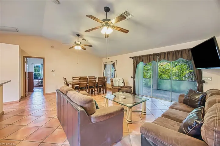 Living area featuring light tile patterned floors, vaulted ceiling, healthy amount of natural light, and a ceiling fan