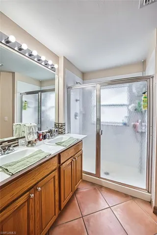 Bathroom featuring a stall shower, light tile patterned floors, double vanity, and healthy amount of natural light