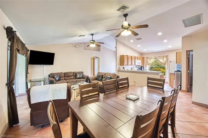 Dining space with light tile patterned floors, lofted ceiling, ceiling fan, arched walkways, and recessed lighting