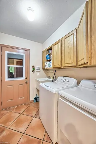 Washroom featuring light tile patterned floors, a textured ceiling, washer and clothes dryer, and cabinet space
