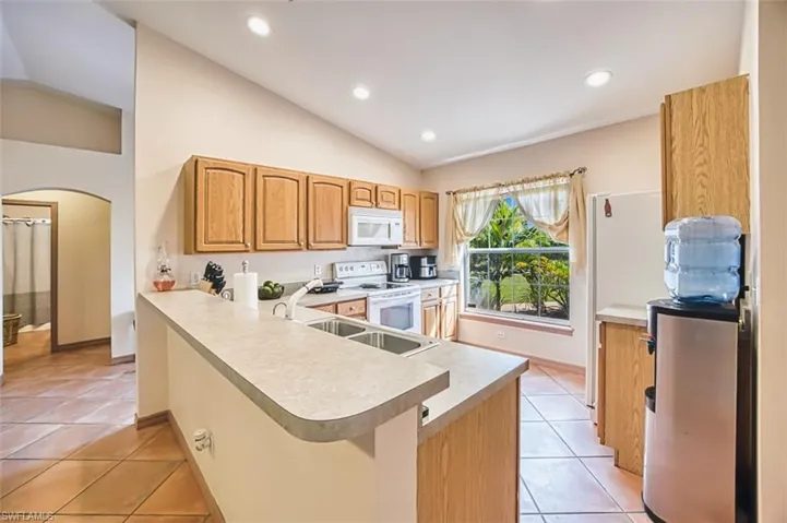 Kitchen featuring lofted ceiling, white appliances, arched walkways, recessed lighting, and light tile patterned floors
