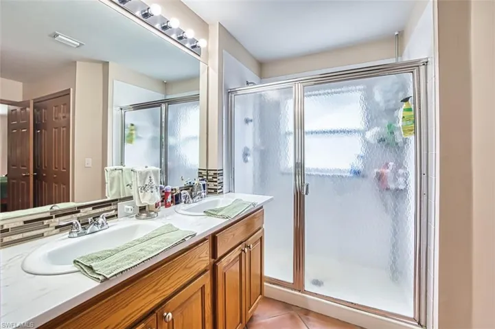 Bathroom with a shower stall, light tile patterned floors, and double vanity