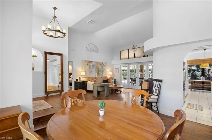 Dining room featuring a chandelier, arched walkways, wood finished floors, vaulted ceiling, and french doors