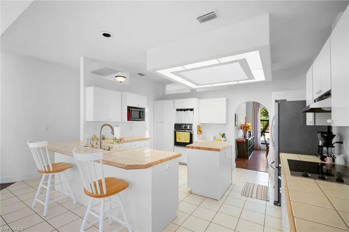 Kitchen featuring arched walkways, a peninsula, white cabinetry, and tile countertops