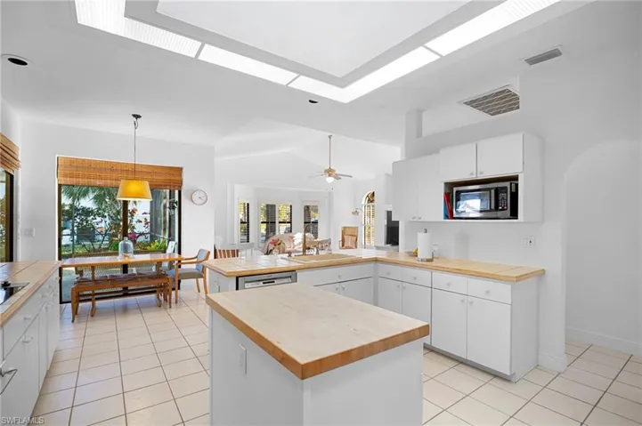 Kitchen with a peninsula, tile counters, white cabinets, hanging light fixtures, and vaulted ceiling