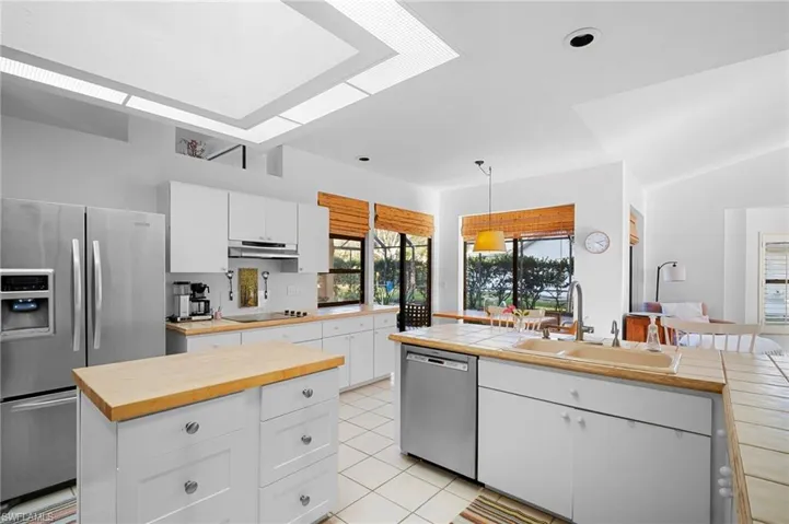 Kitchen with white cabinetry, stainless steel appliances, hanging light fixtures, light tile patterned flooring, and a kitchen island
