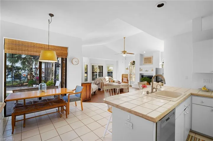 Kitchen with a peninsula, a fireplace, tile counters, stainless steel dishwasher, and white cabinetry