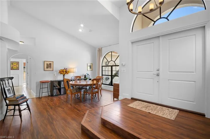 Entrance foyer with vaulted ceiling, dark wood-type flooring, a chandelier, and arched walkways