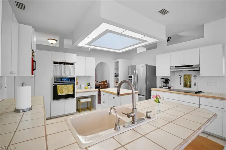 Kitchen with tile counters, white cabinets, black appliances, a skylight, and a kitchen island