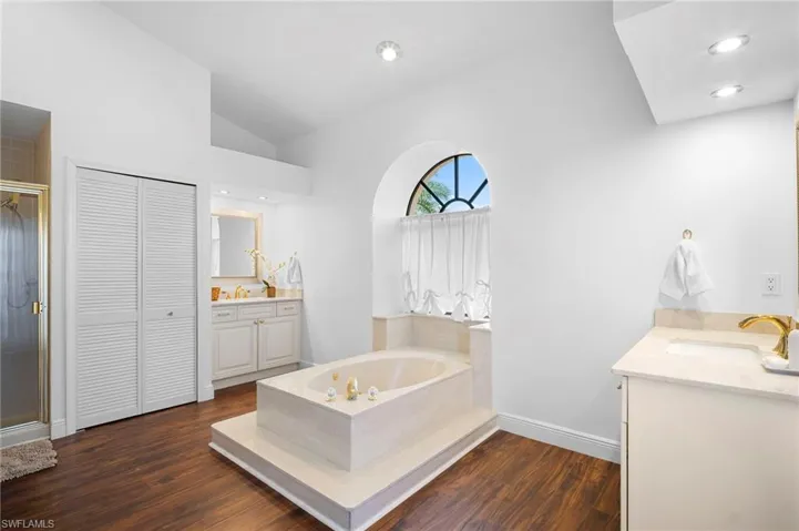 Bathroom with two vanities, a closet, vaulted ceiling, dark wood-style flooring, and a shower stall