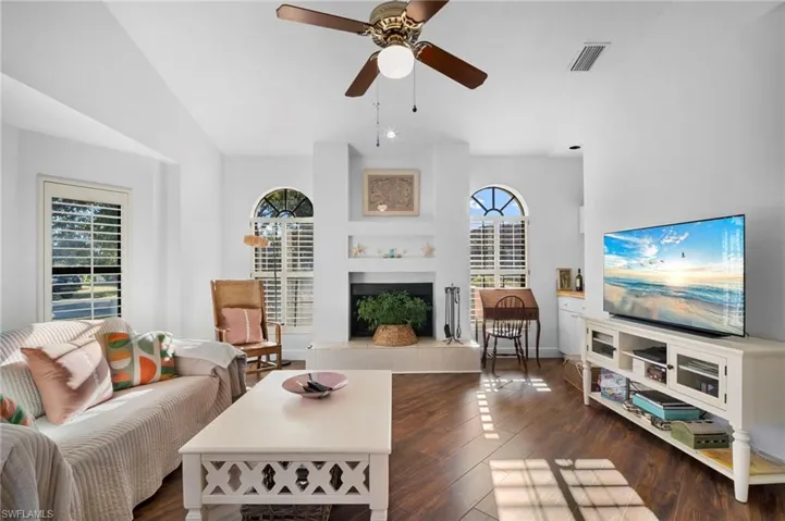 Living area with hardwood / wood-style flooring, ceiling fan, a tiled fireplace, and a high ceiling