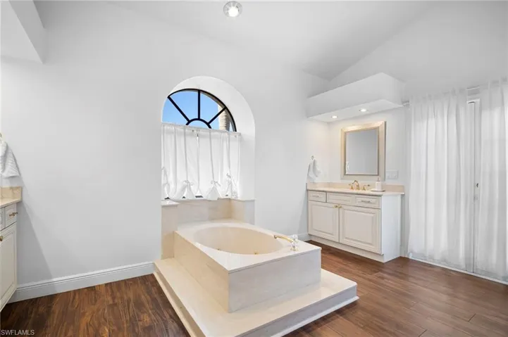 Bathroom featuring vanity, a tub with jets, vaulted ceiling, and dark wood-style flooring
