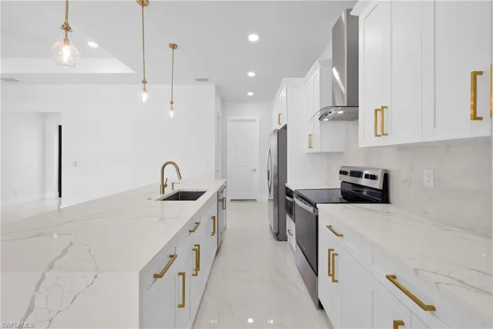 Kitchen with sink, appliances with stainless steel finishes, white cabinetry, pendant lighting, and wall chimney range hood