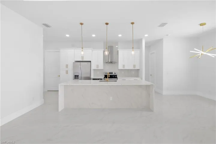 Kitchen with light tile patterned floors, backsplash, stainless steel refrigerator with ice dispenser, and wall chimney exhaust hood