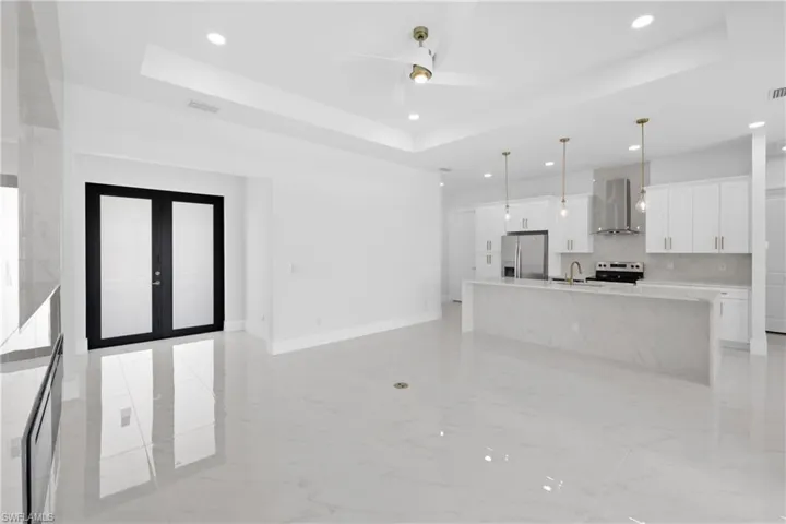 Kitchen with a tray ceiling, stainless steel fridge, wall chimney range hood, and french doors