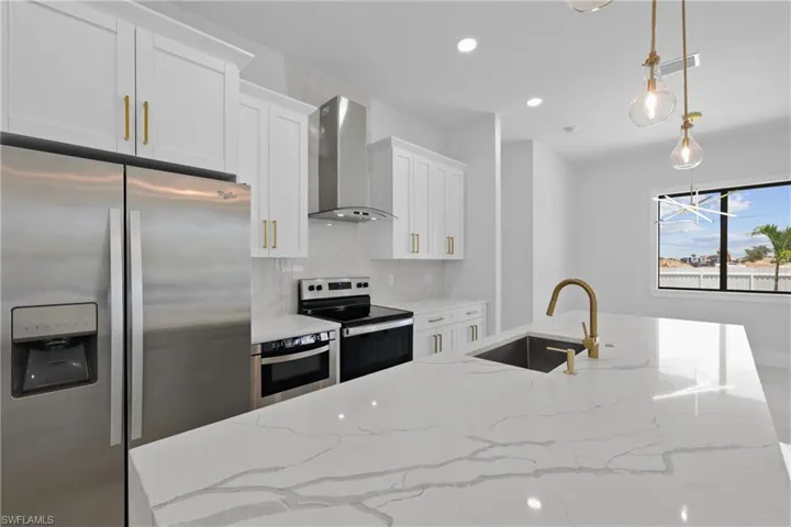 Kitchen featuring sink, decorative light fixtures, appliances with stainless steel finishes, light stone counters, and wall chimney range hood
