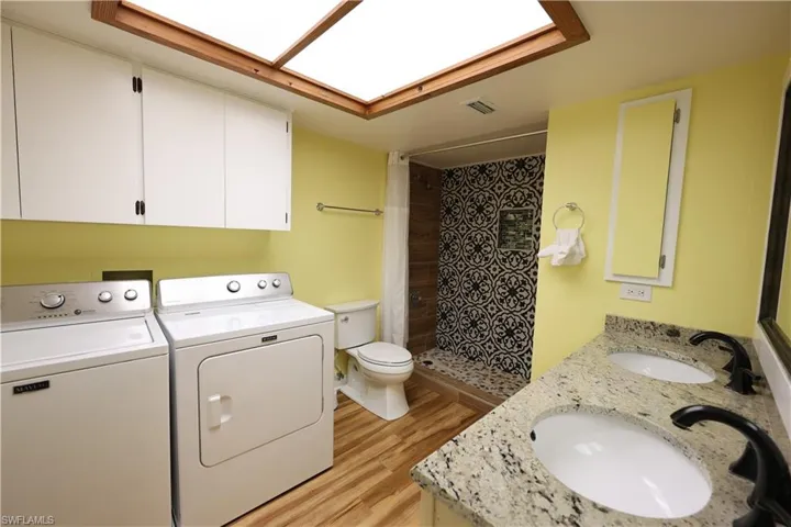 Full bathroom with light wood-style floors, a shower stall, double vanity, washer and clothes dryer, and a skylight