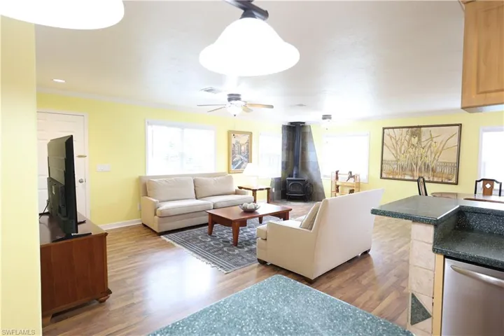 Living room featuring a wood stove, dark wood-type flooring, ornamental molding, and ceiling fan